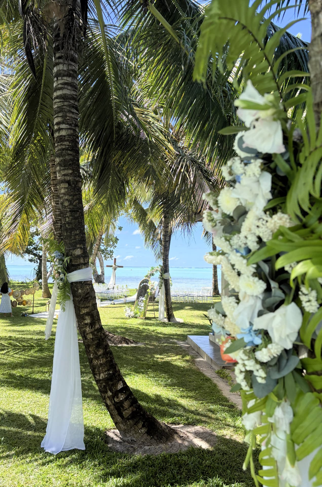 Palm trunks draped in white fabric and flowers leading to a beachside ceremony