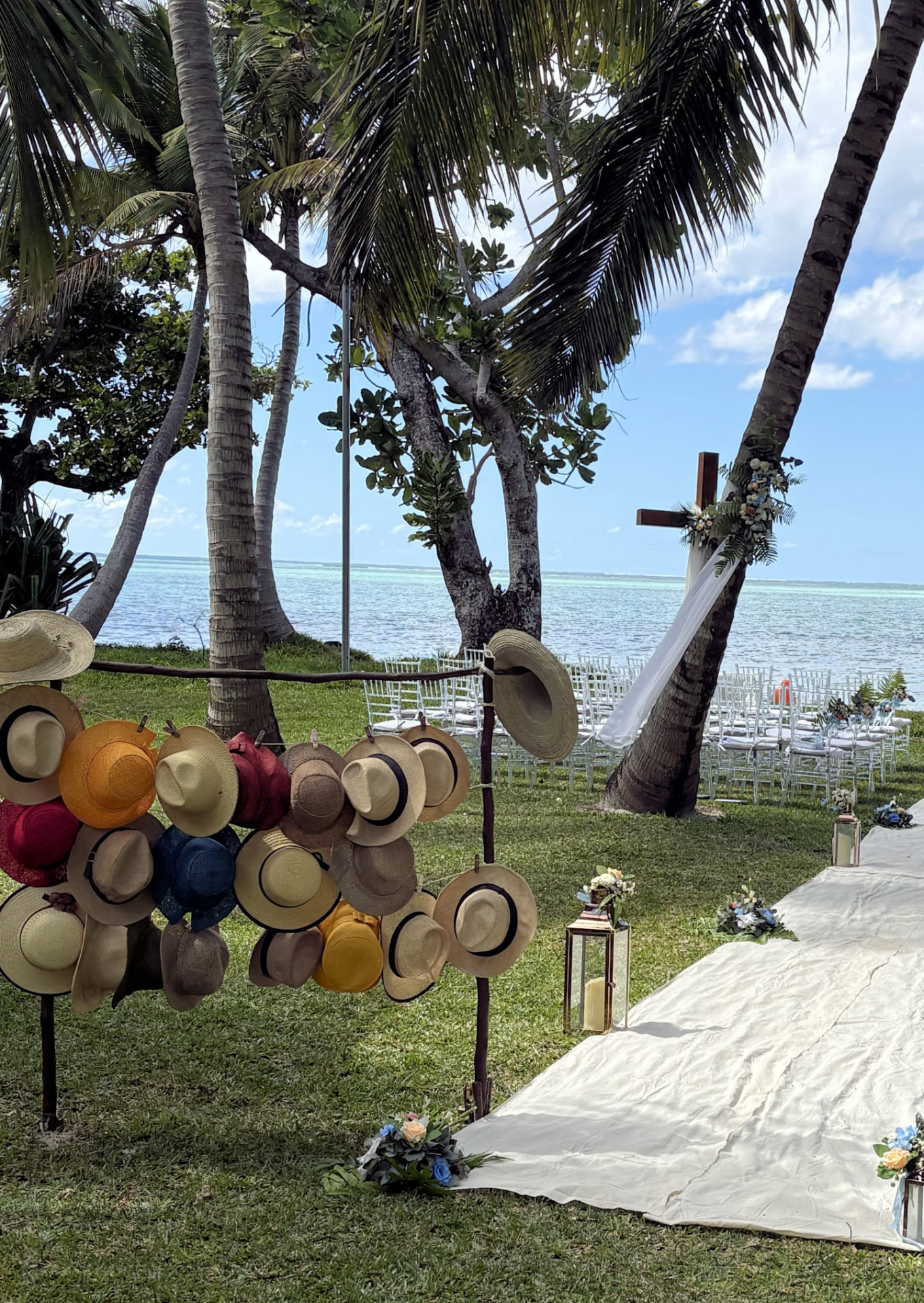 Ceremony aisle and chairs beneath the coconut palms with a display of sun hats for guests